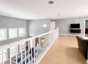 A spacious living area with a high ceiling, a white railing, and a flat-screen TV mounted on the wall. - Oasis in Da Valley | Elegant 5-Bedroom Getaway (Douglasville)