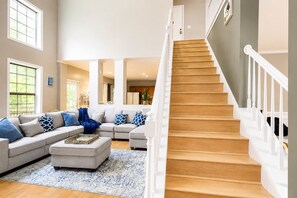 A spacious living room with a large sectional sofa, a wooden staircase, and a view of the kitchen. - Oasis in Da Valley | Elegant 5-Bedroom Getaway (Douglasville)