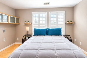 A bedroom with a bed, two nightstands, a lamp, and two windows with shutters. - Oasis in Da Valley | Elegant 5-Bedroom Getaway (Douglasville)