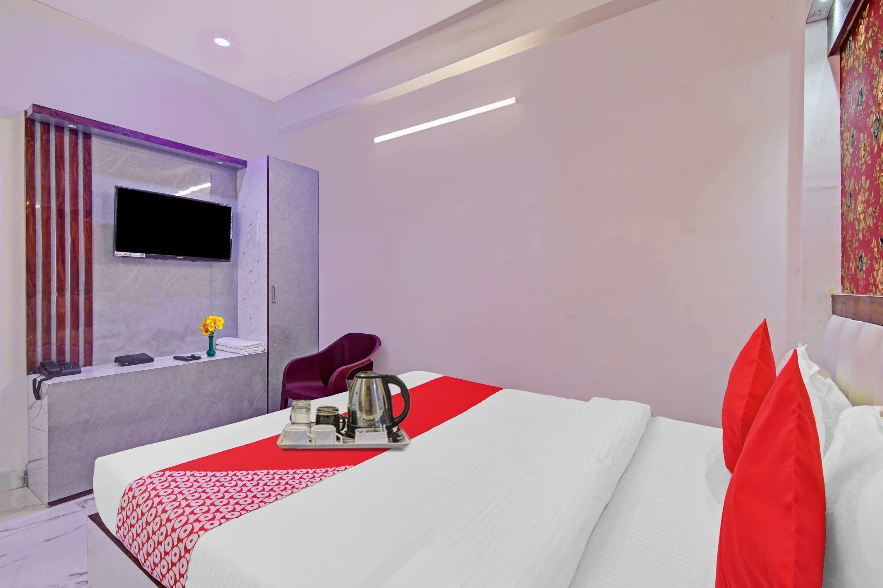 Una habitación de hotel moderna con una cama grande, un televisor de pantalla plana montado en la pared, una zona de estar pequeña y una ventana con cortinas.
