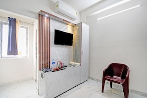 A hotel room with a marble vanity, a mounted flat-screen TV, a red chair, and a window with curtains. - Hotel O Diamond Regency (Kolkata)