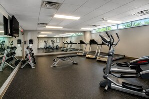 Une salle de sport équipée de tapis de course, d’appareils de musculation et d’un mur recouvert de miroirs.