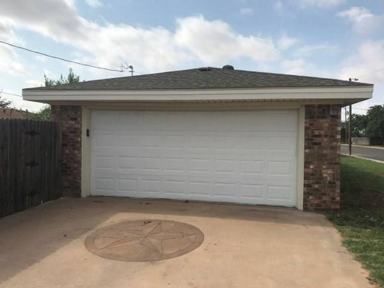 A single-story house with a garage door, a brick foundation, and a concrete driveway.