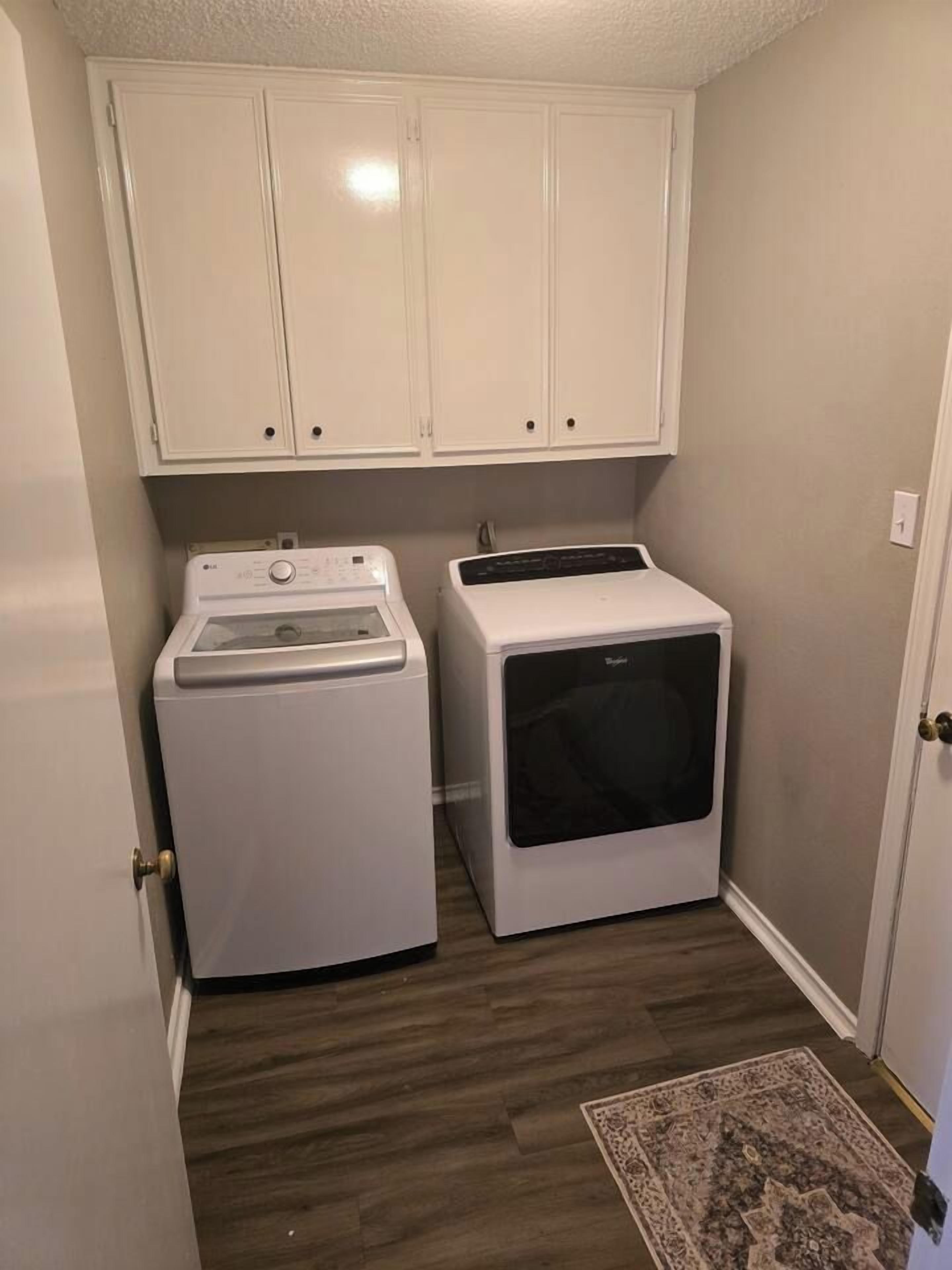 Een wasserette met een wasmachine en droger, houten vloeren en een gekleurd vloerkleed.