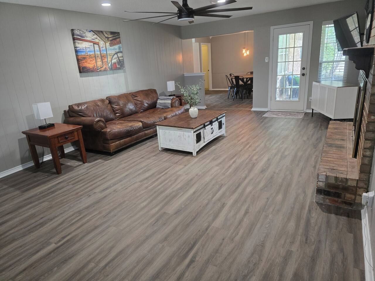 A spacious living room with a brown leather sofa, a white coffee table, and a ceiling fan.