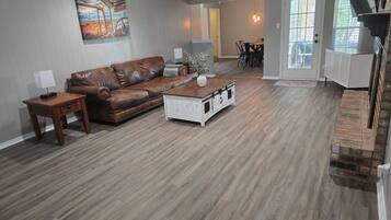 A spacious living room with a brown leather sofa, a white coffee table, and a ceiling fan.