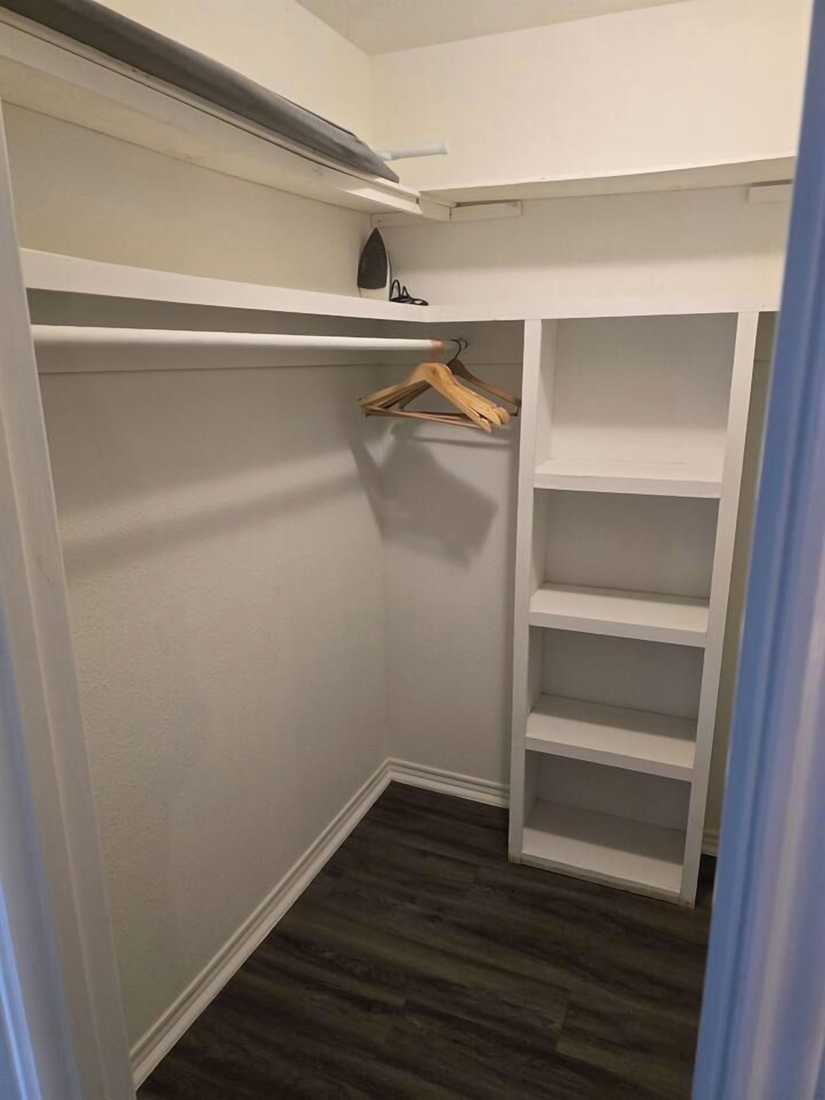 A walk-in closet with white shelving units and a wooden hanger rod.
