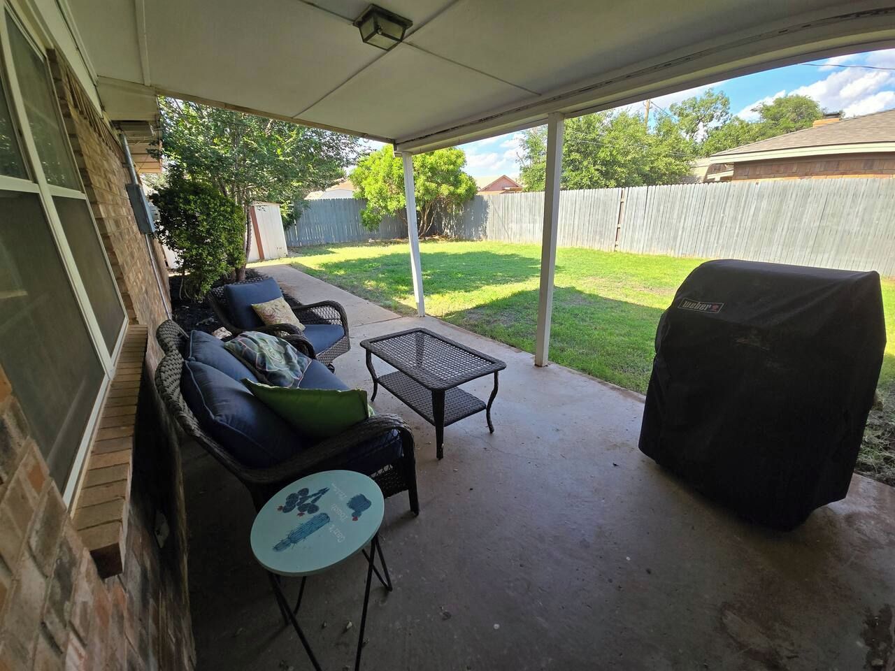 A covered patio with a grill, outdoor furniture, and a view of the backyard.