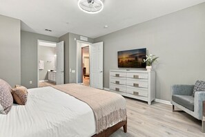 A bedroom with a bed, a dresser, a chair, and a painting on the wall. - Luxury 3BR Newly Renovated Lake View Vista Cay (Orlando)
