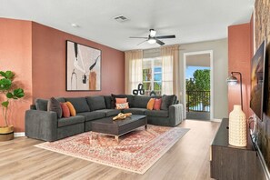 A modern living room with a sectional sofa, a coffee table, a large painting, and a view to the outdoors. - Luxury 3BR Newly Renovated Lake View Vista Cay (Orlando)