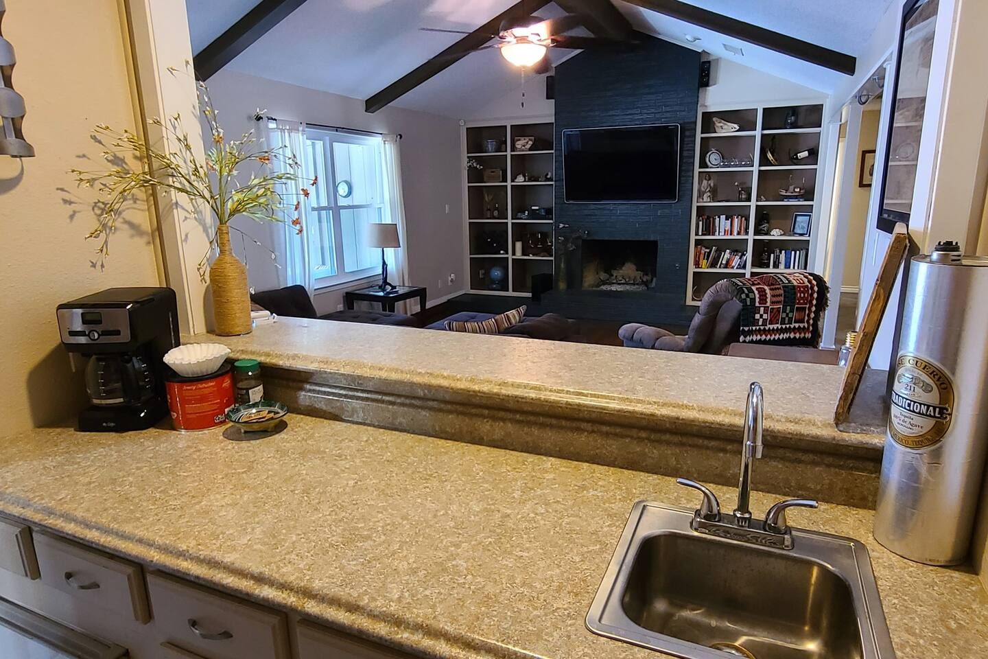 A kitchen with a granite countertop, a coffee maker, a jar of jam, and a stainless steel refrigerator.