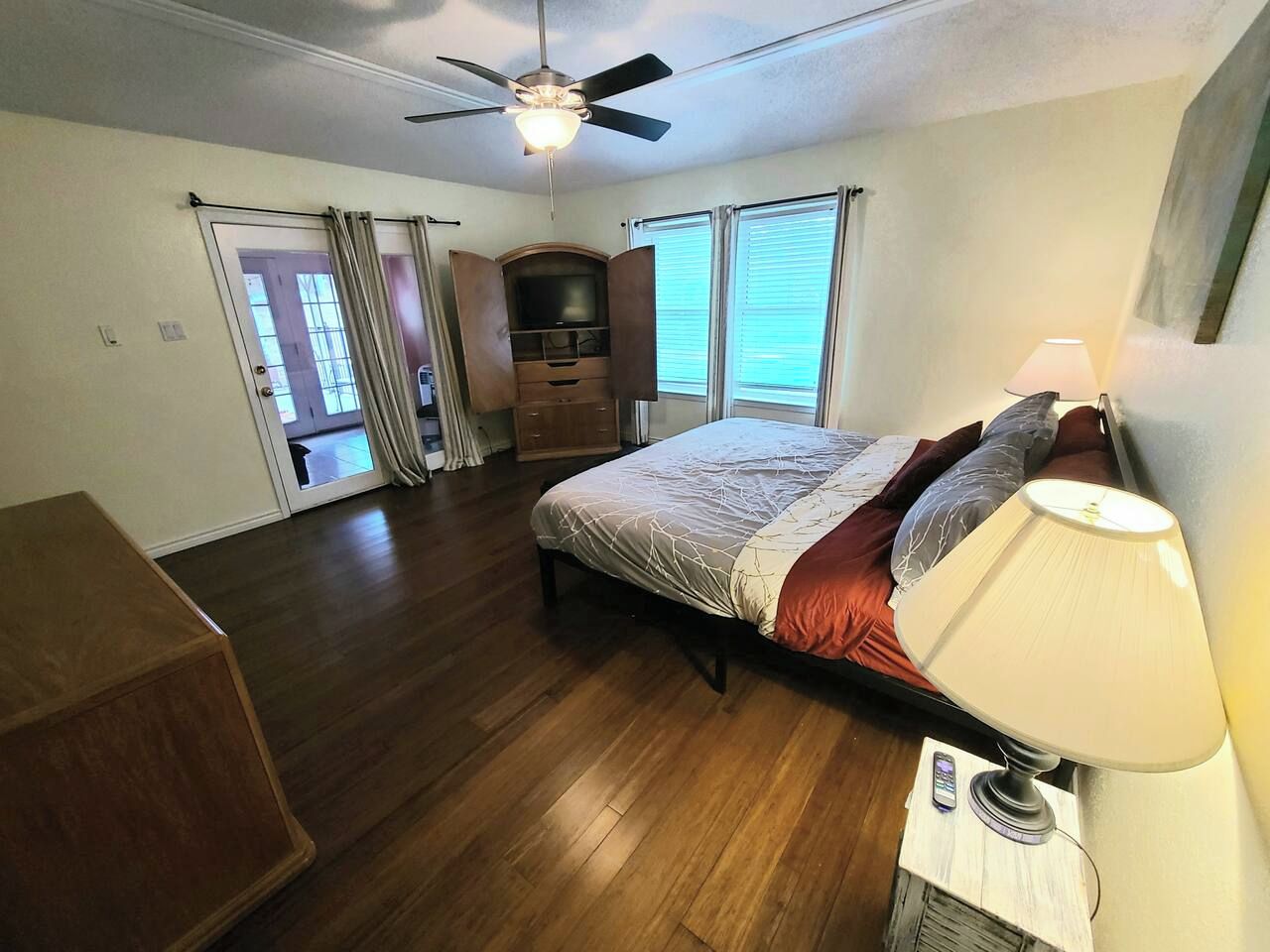 A bedroom with a bed, a ceiling fan, a lamp, and a TV.