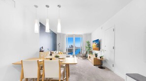 Un salon moderne avec un coin repas, de grandes fenêtres et une vue sur un plan d’eau.