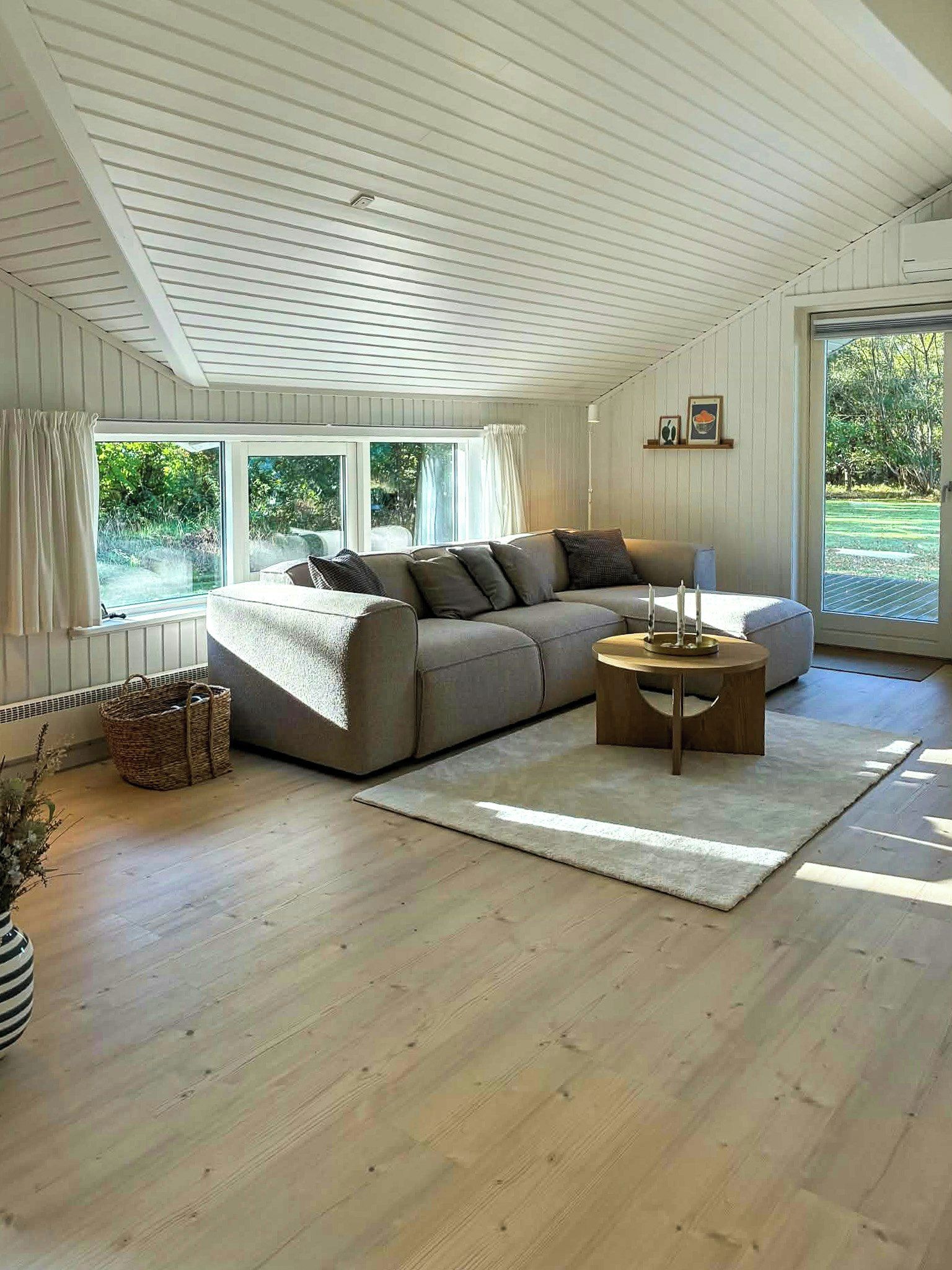 A spacious living room with a large sectional sofa, a round coffee table, and a view of the outdoors through large windows.