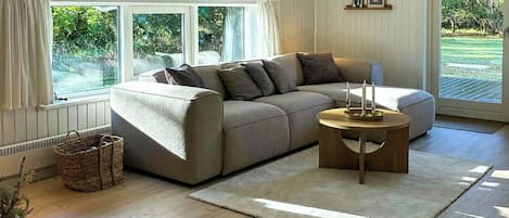 A spacious living room with a large sectional sofa, a round coffee table, and a view of the outdoors through large windows.