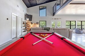 A pool table in a modern living room with a high ceiling and large windows. - Xenia Ranch Barndo l Pool HotTub l Partial House (Valley Mills)