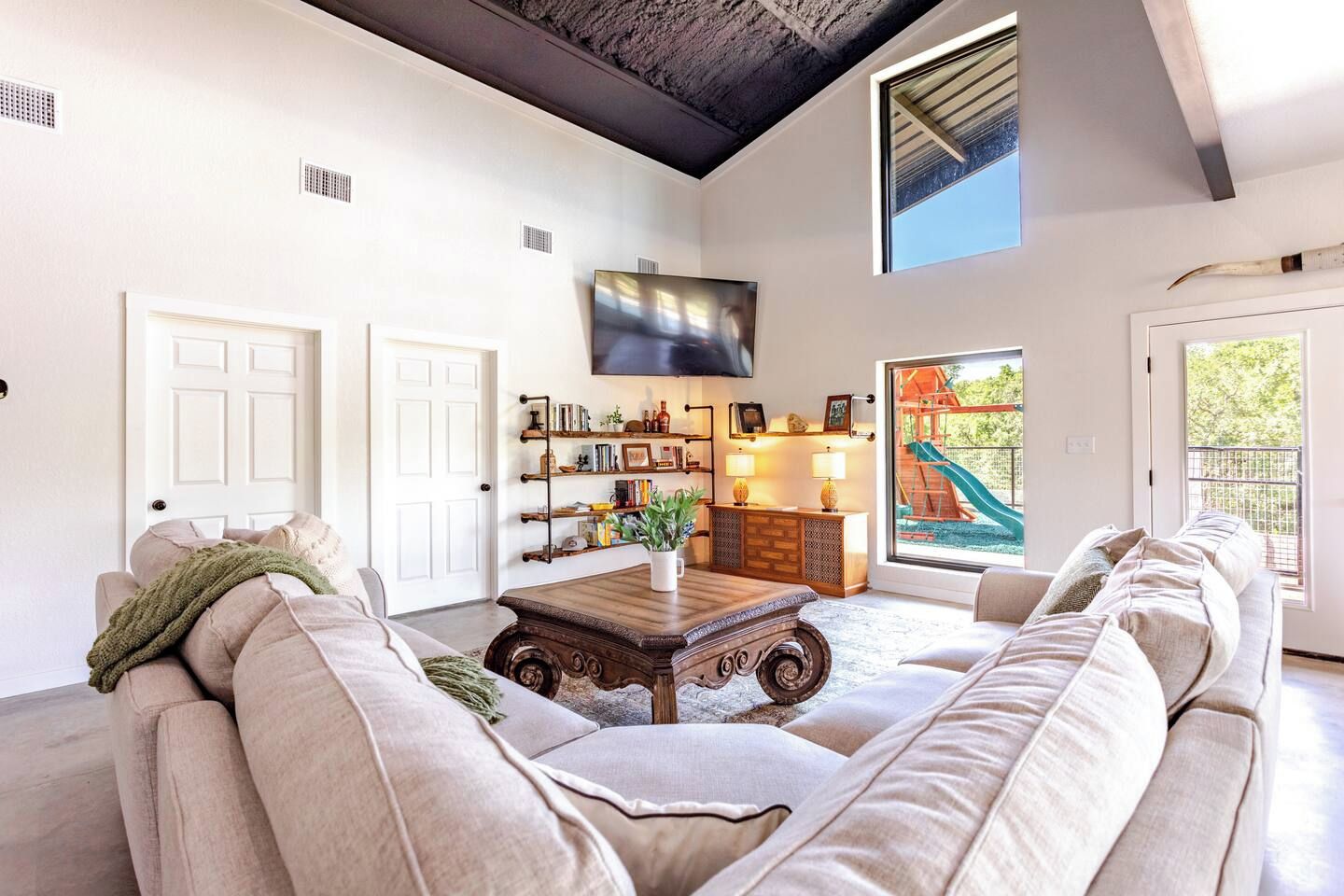 A spacious living room with a large sofa, a coffee table, and a bookshelf. There is a sliding glass door leading to an outdoor area with a slide.