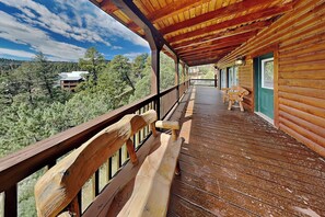 Um deck de madeira com um banco e vista para uma área arborizada.