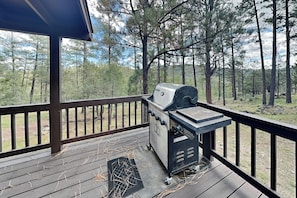 A covered outdoor area with a barbecue grill and a view of a forest. - Gonzo Chalet (Ruidoso)