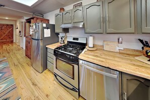 A kitchen with stainless steel appliances, wooden flooring, and light-colored cabinets. - Gonzo Chalet (Ruidoso)