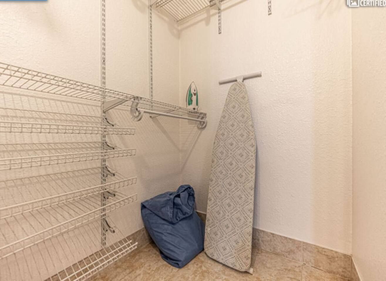 A laundry area with metal shelves, a hanging iron, and a blue bag.