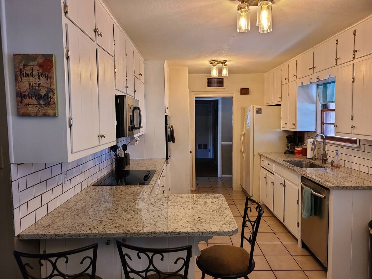 A kitchen with white cabinets, granite countertops, and a dining area with a chair.