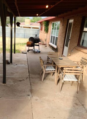 Eine Terrasse im Freien mit Betonboden, einem Holztisch mit Stühlen und einem Grill.