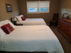 Ein Zimmer mit zwei Betten, einem Schminktisch, einem Stuhl und einem Fenster mit Jalousien.