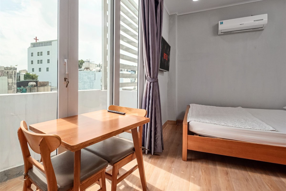 Une pièce comprenant un bureau en bois, deux chaises, un lit, un téléviseur fixé au mur et un appareil de climatisation.