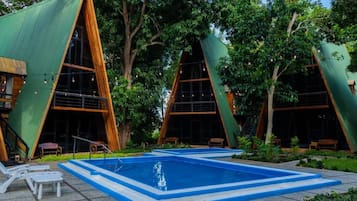 A modern building with a triangular roof design, a swimming pool, and outdoor seating.