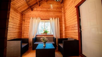 Une chambre de style rustique, avec un plafond en bois, une fenêtre avec des rideaux, un canapé, deux fauteuils et une petite table sur laquelle est posé un vase.