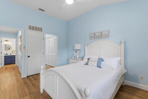A bedroom with a white bed, a nightstand, a lamp, and a wall with framed pictures. - Seaside Veranda (New Smyrna Beach)