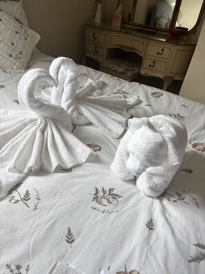 A bed with white towels arranged in a bow shape, a floral-patterned bedspread, and a dresser with a mirror and a vase. - Charming Cottage near Bicester Village & Oxford (Piddington)