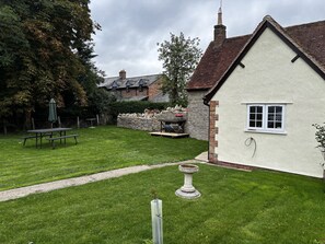 A well-maintained garden with a stone wall, a picnic table, and a birdbath. - Charming Cottage near Bicester Village & Oxford (Piddington)