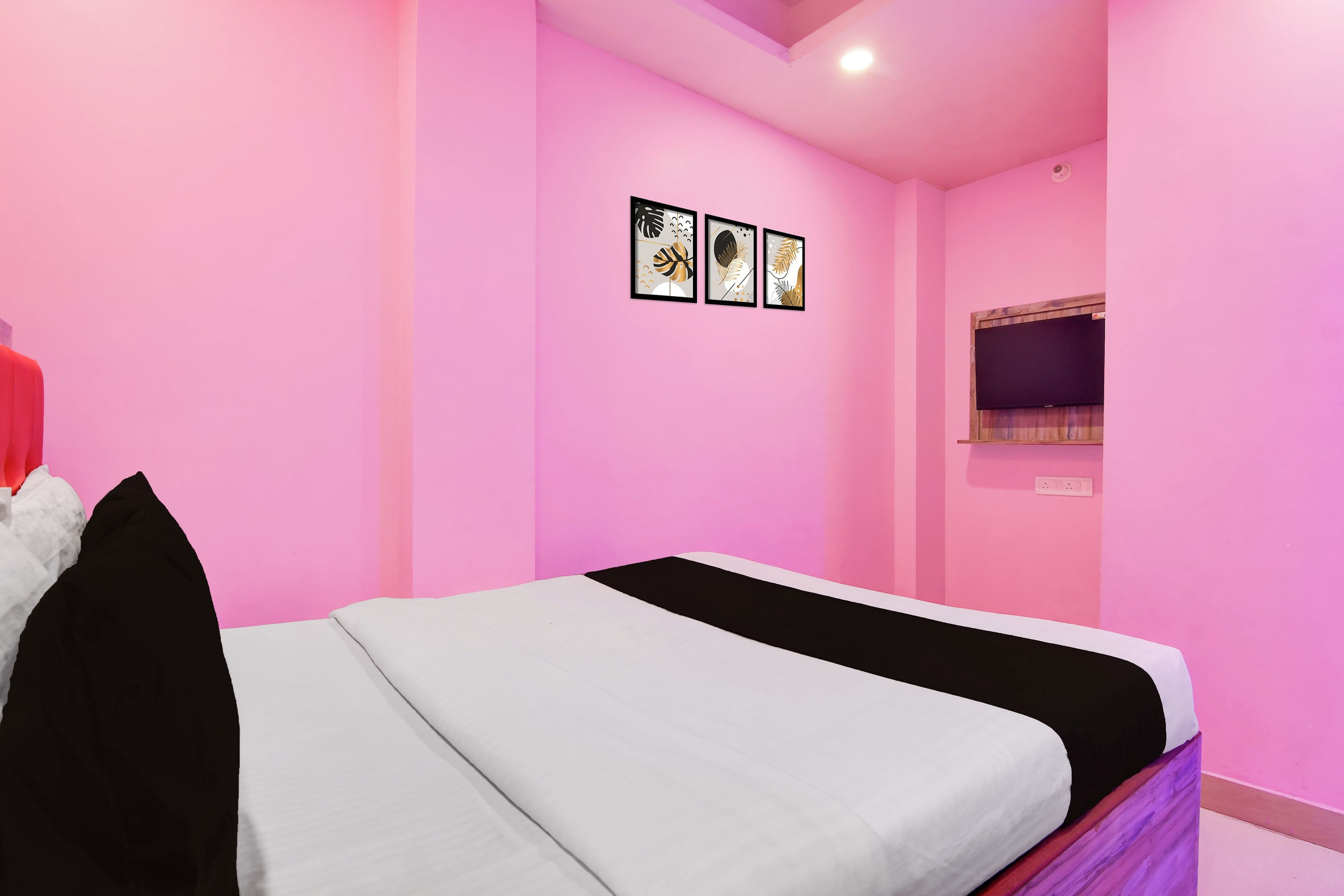Una habitación con una cama, un televisor montado en la pared y tres cuadros enmarcados.