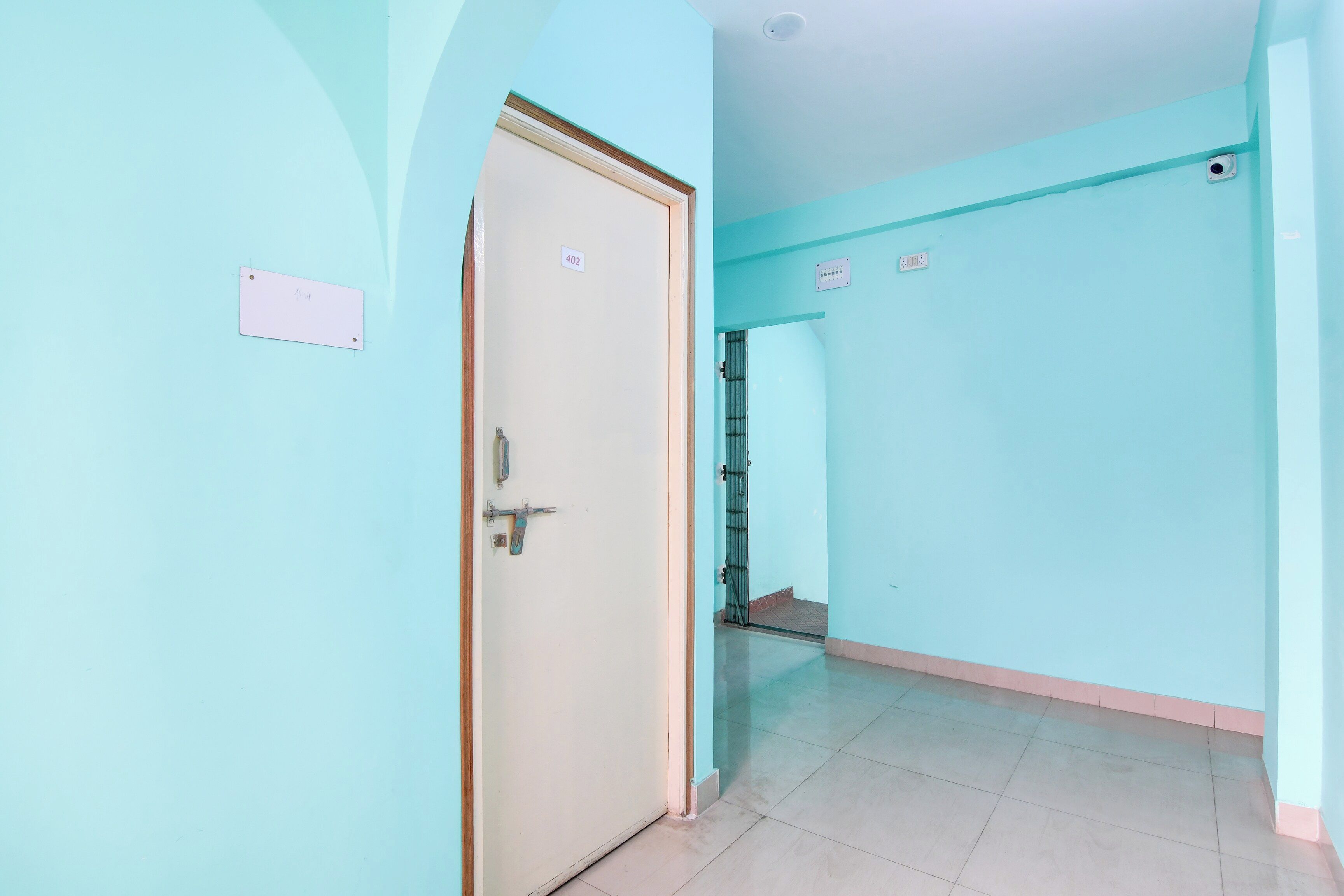 Um corredor com uma porta fechada, parede azul clara e chão de azulejos.