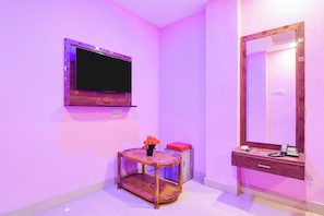 Una habitació amb televisió de pantalla plana penjada a la paret, un tocador de fusta amb mirall i una taula petita amb un ram de flors.