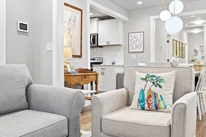 A modern living room with grey sofas, a wooden coffee table, and a kitchen in the background. - Coastal Charm in Downtown Wilmington 2BR, Walk to Dining & Riverfront (Wilmington)
