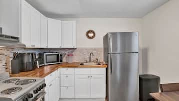 A compact kitchen with white cabinets, a stainless steel refrigerator, a microwave, a stove, and a sink.