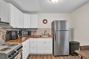 A compact kitchen with white cabinets, a stainless steel refrigerator, a microwave, a stove, and a sink. - Michigan In Mobile (Mobile)