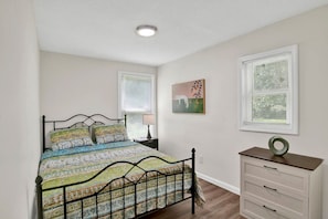 A bedroom with a bed, a dresser, a nightstand, a window with blinds, and a ceiling light. - Michigan In Mobile (Mobile)