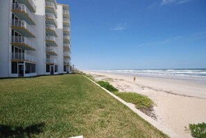 Ein Strandhotel mit mehreren Balkonen, einer Rasenfläche und einem Sandstrand.