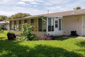 A single-story house with a covered porch, a front door, and a small front yard with grass and shrubs. - Pet friendly home with large backyard (New Smyrna Beach)