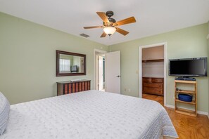 A bedroom with a bed, a ceiling fan, a television, a wardrobe, and a mirror. - Pet friendly home with large backyard (New Smyrna Beach)