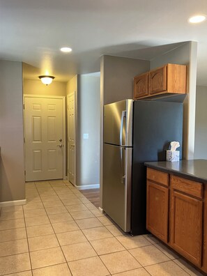 A kitchen with a stainless steel refrigerator, wooden cabinets, and a tiled floor.