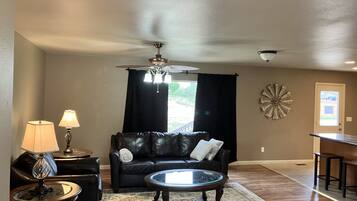 A living room with a black leather sofa, a glass coffee table, and a chandelier.