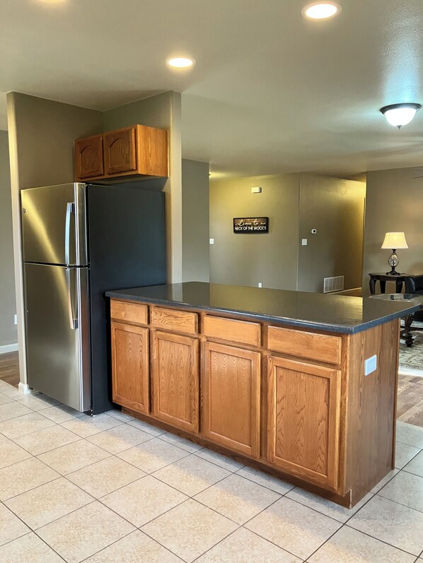 A kitchen with a stainless steel refrigerator, wooden cabinets, and a black countertop island.