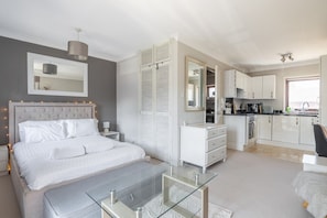 A bedroom with a bed, bedside tables, a glass coffee table, a wardrobe, and a mirror. - Charming 3-Bed Home with Garden and Parking (Cambridge)