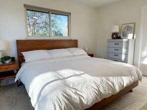 A bedroom with a large bed, a dresser, a nightstand, and a window with a view of trees. - Spacious Boulder Home Perfect for Sundance - Near CU, Downtown, & Boulder Trails (Boulder)