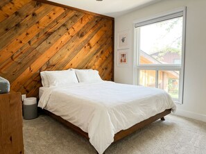 Un dormitorio con cabecera de listones de madera, una ventana grande y una cama con ropa blanca.